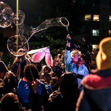 A photo from Winter Lights - children look on as an adult blows large bubbles in the air in the Urban Park. Photo by Edward Felton.